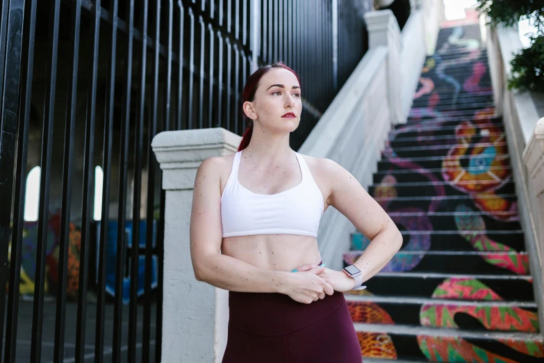a woman standing in front of a set of stairs, inspired by Sydney Carline, pexels contest winner, sports bra, train with maroon, lachlan bailey, pale-skinned