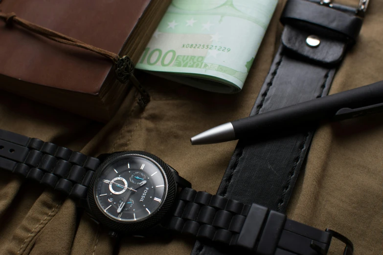 a watch sitting on top of a table next to a pen, a still life, inspired by Eugène Brands, pexels contest winner, all black matte product, cash on a sidetable, fossil, close up shot a rugged