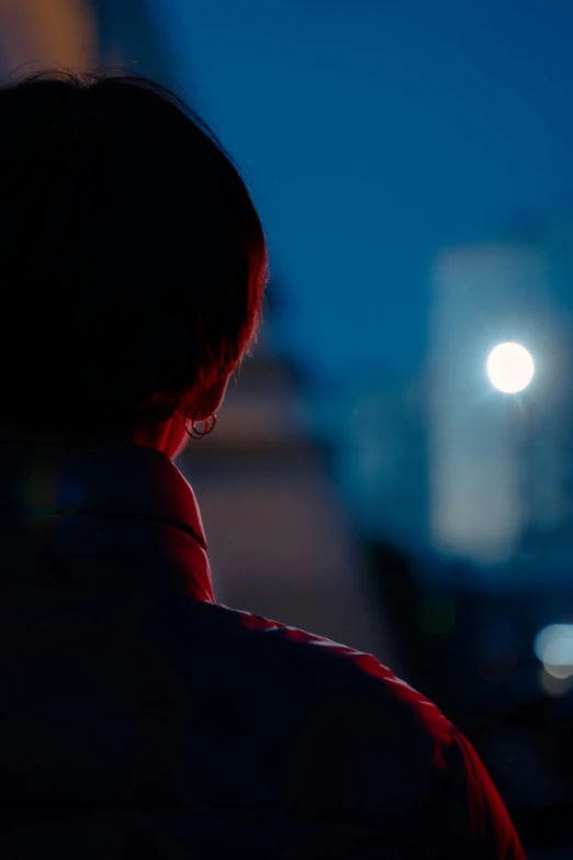 a person standing in front of a building at night, looking off into the distance, close-up shot from behind, pondering, red and blue lighting