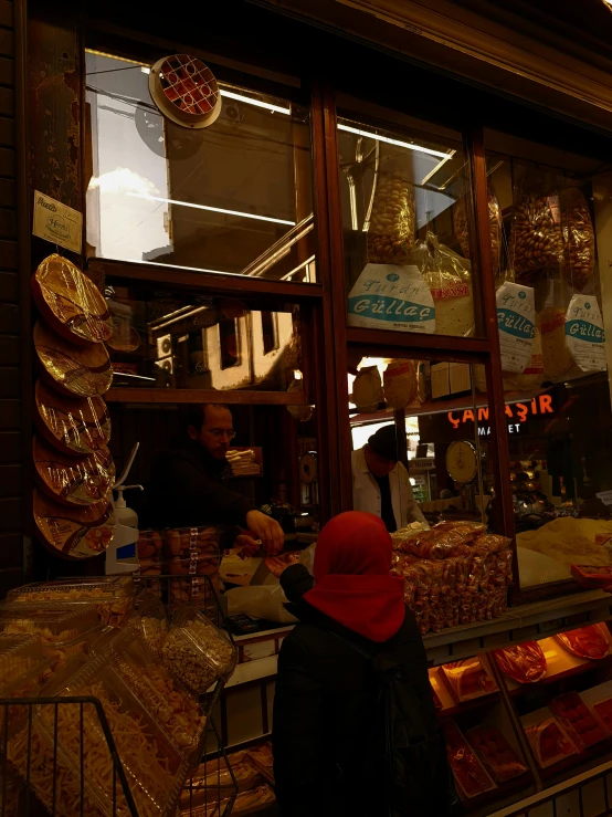 a woman in a red hat standing in front of a store, by Jan Tengnagel, pexels contest winner, art nouveau, having a snack, dark and beige atmosphere, gold, medium shot taken from behind