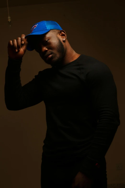 a man in a black shirt and a blue hat, an album cover, inspired by Paul Georges, trending on pexels, ( ( dark skin ) ), masculine pose, burly man, actor