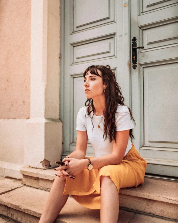 a woman sitting on the steps of a building, inspired by Valéria Dénes, trending on pexels, ocher, portrait image, leaning on door, oona chaplin