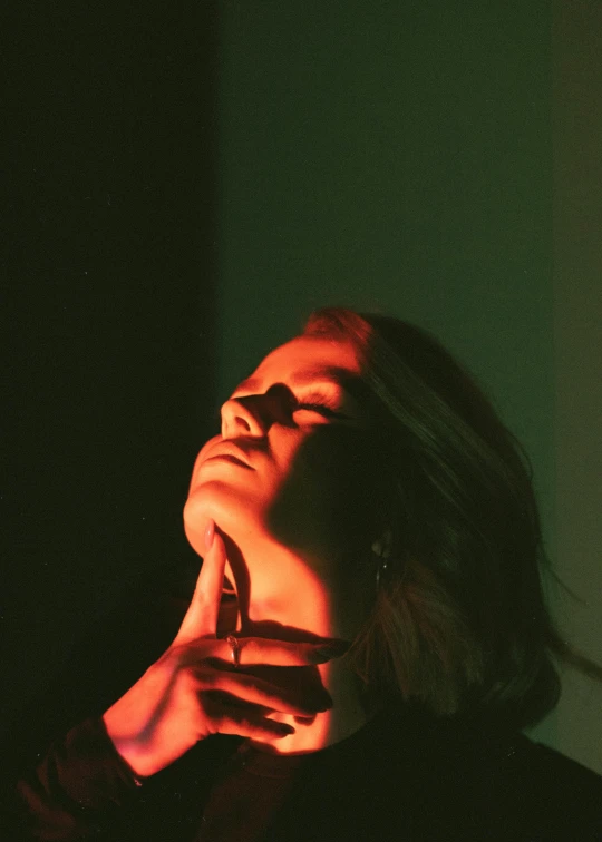 a close up of a person holding a cell phone, an album cover, inspired by Elsa Bleda, photorealism, young woman looking up, glowing with colored light, hand on her chin, redscale photography