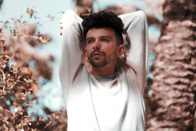 a man standing in front of a palm tree, an album cover, pexels contest winner, mannerism, wearing a white sweater, julian calle, in front of a forest background, pastel faded effect