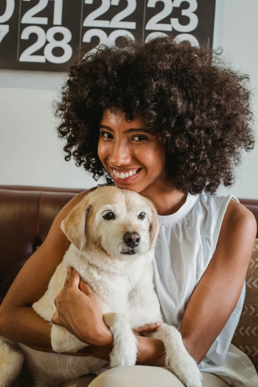 a woman sitting on a couch holding a dog, a portrait, trending on unsplash, short blonde afro, with brown skin, dark short curly hair smiling, thumbnail