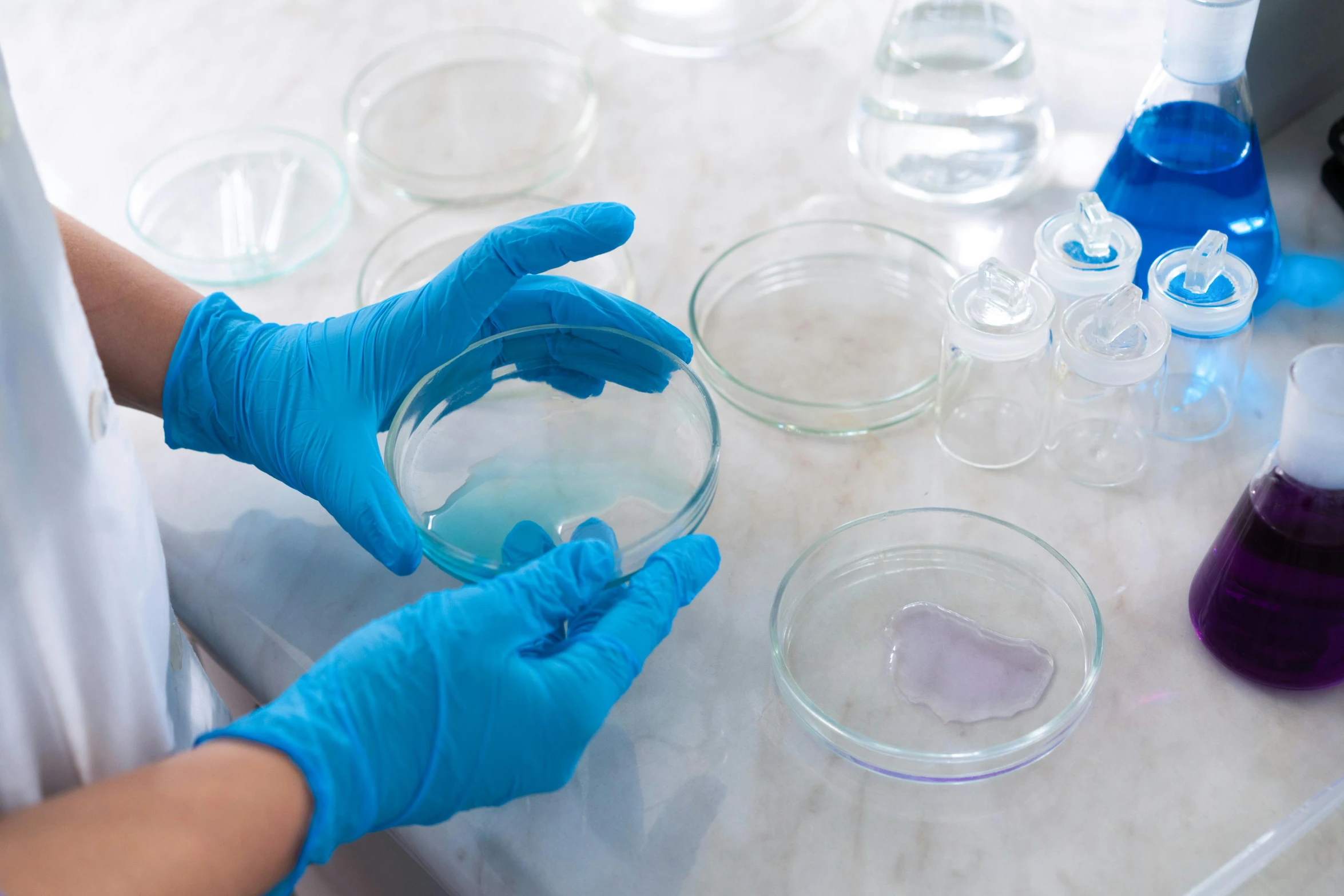 a person in blue gloves holding a bowl of liquid, shutterstock, process art, scientific specimens, high samples, silicone cover, soft coloured gel lighting