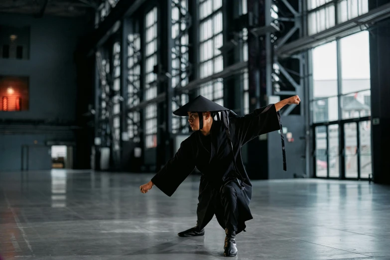 a man in a black robe and hat doing a trick on a skateboard, inspired by Ma Quan, pexels contest winner, visual art, wearing hakama, standing in a large empty hall, photograph of a techwear woman, kung fu