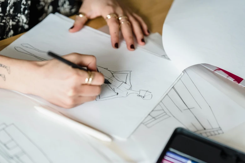 a woman sitting at a table drawing on a piece of paper, a drawing, trending on pexels, costume design made with love, 9 9 designs, tailored clothing, building plans