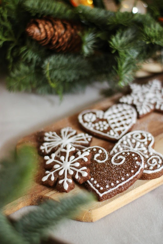 a wooden cutting board topped with cookies on top of a table, folk art, light snow, intricate filigree, heart, medium close up