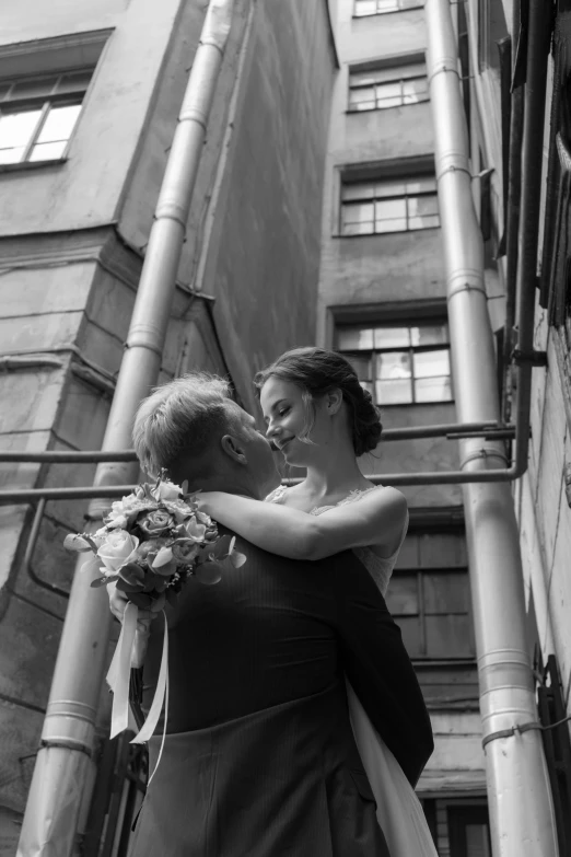 a bride and groom kissing in front of a tall building, a black and white photo, by Tamas Galambos, 15081959 21121991 01012000 4k, standing in an alleyway, vladimir krisetskiy, recital