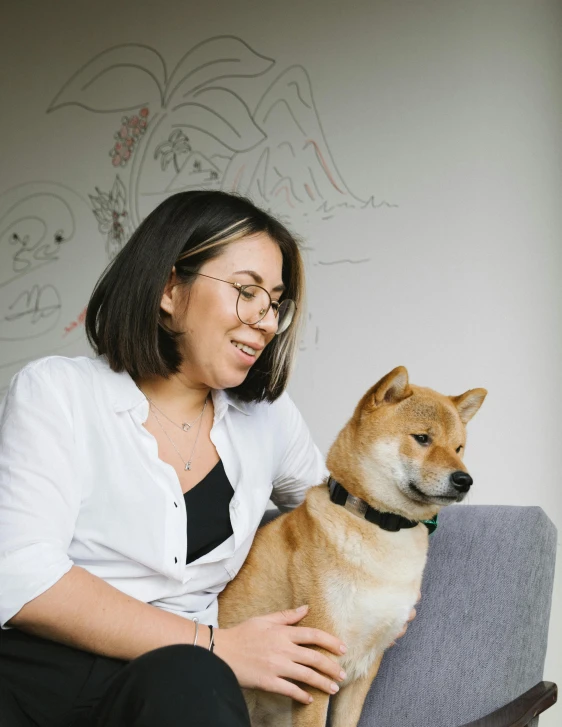 a woman sitting on a chair with a dog, a cartoon, inspired by Shiba Kōkan, trending on unsplash, on a couch, small chin, slightly smiling, taken in the late 2010s