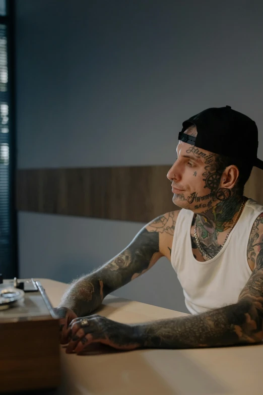 a man with tattoos sitting at a table, inspired by Seb McKinnon, sitting behind desk, epk, hotel room, medium head to shoulder shot