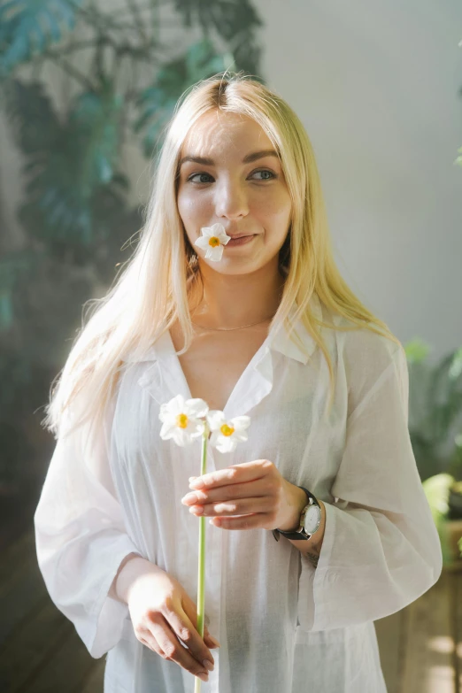 a woman holding a flower in front of her face, with white long hair, wearing a linen shirt, sydney sweeney, white clothing