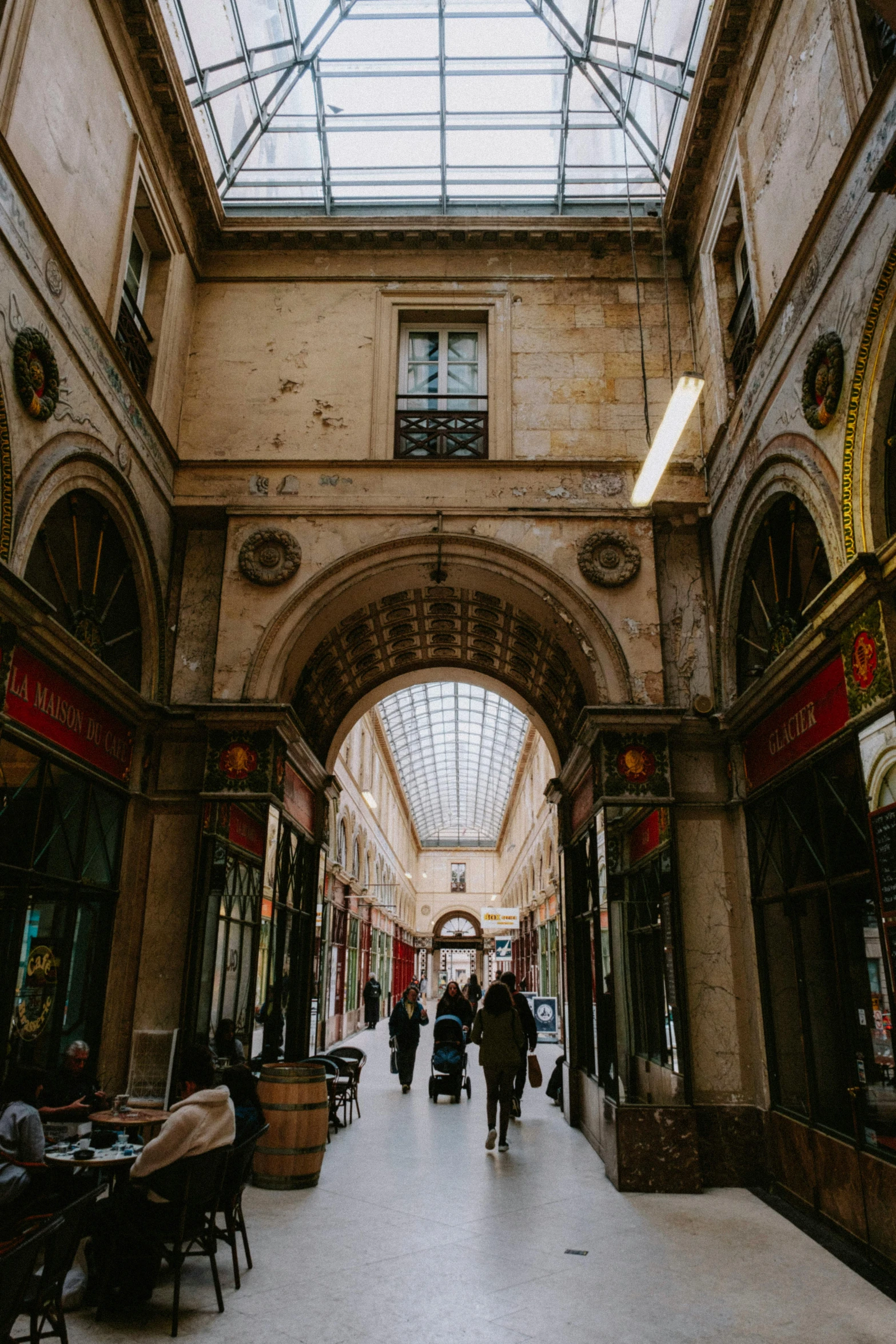 a group of people sitting at tables inside of a building, an archway, an alley in paris in winter, malls, gorgeous buildings