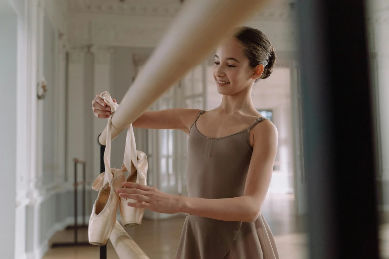 a woman in a brown dress holding a pair of ballet shoes, pexels contest winner, arabesque, avatar image, schools, smiling and dancing, straps