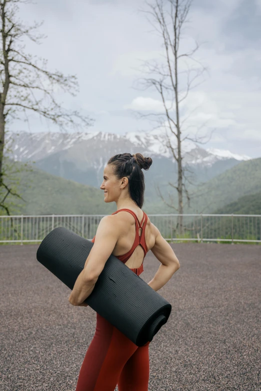 a woman holding a yoga mat in a parking lot, by Anna Haifisch, mountainous setting, russia, high quality photo, taiwan