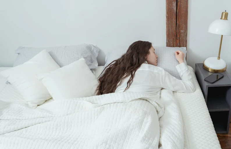 a woman laying in bed under a blanket, happening, white and grey, facing away, beds, bedhead