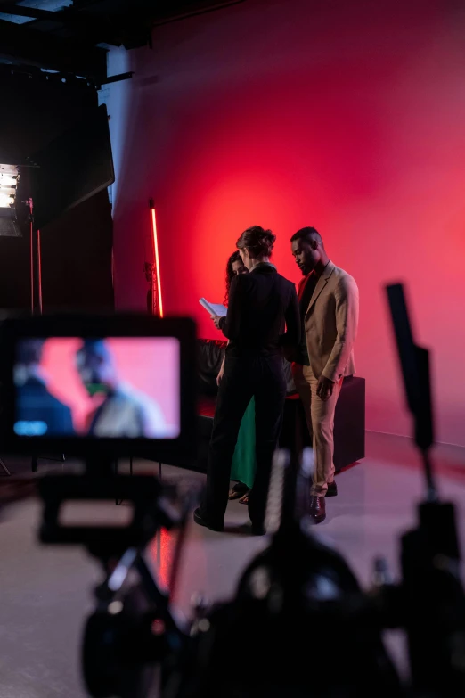 a couple of people that are standing in front of a camera, trending on pexels, video art, red and cinematic lighting, at a fashion shoot, giving an interview, long shot from the back