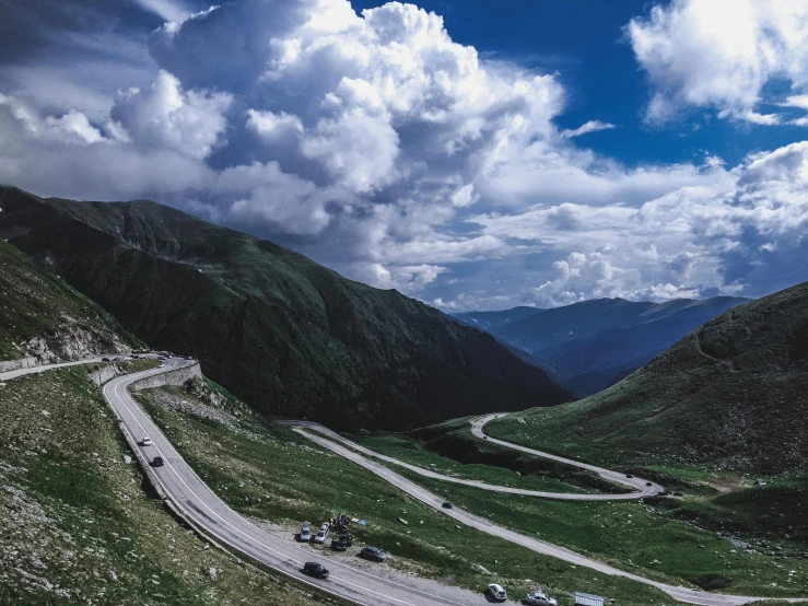 a group of cars driving down a winding road, by Alessandro Allori, pexels contest winner, les nabis, alpine scenery, 1990's photo, skies, fan favorite