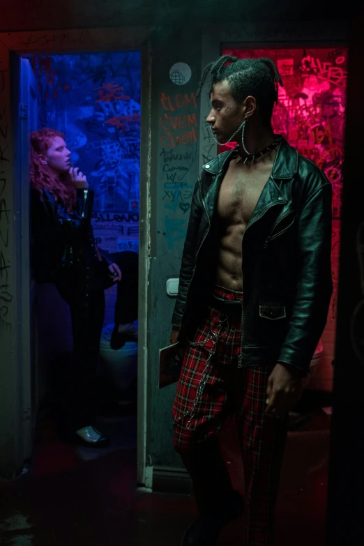 a man in plaid pants and a leather jacket, cyberpunk art, inspired by Nan Goldin, trending on pexels, two models in the frame, in doors, scene from a rave, ariel perez