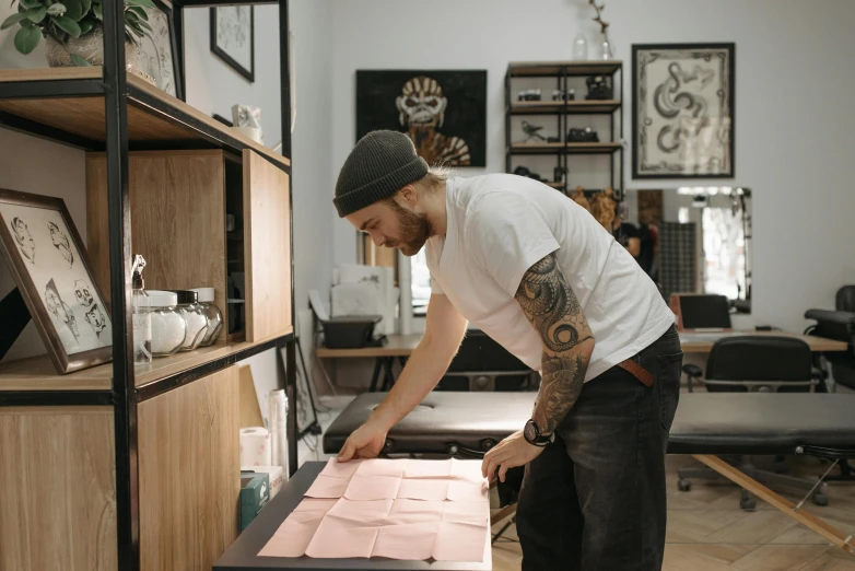 a man that is standing in front of a table, a silk screen, 9 9 designs, tattoo, high quality paper, parchment paper