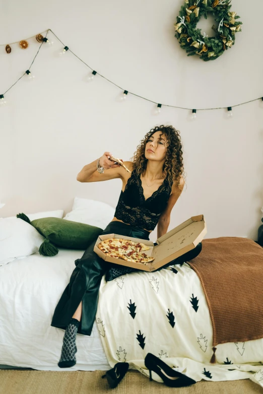 a woman sitting on a bed eating pizza, by Julia Pishtar, trending on pexels, fine art, brown curly hair, college, black, proud looking