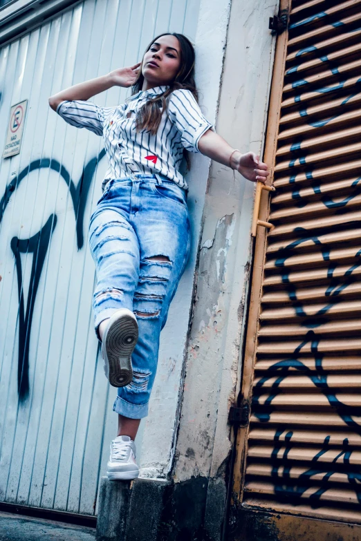 a woman leaning against a wall with graffiti on it, trending on pexels, wearing stripe shirt, leaping towards viewer, ripped jeans, full frame image