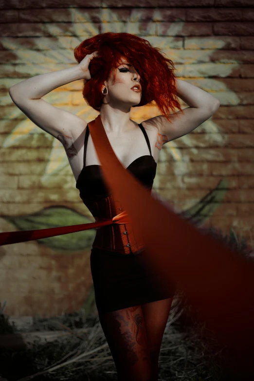 a woman in a black dress holding a red ribbon, inspired by Nan Goldin, pexels contest winner, conceptual art, vibrant red hair, black leather harness, sultry and beckoning, 5 feet away