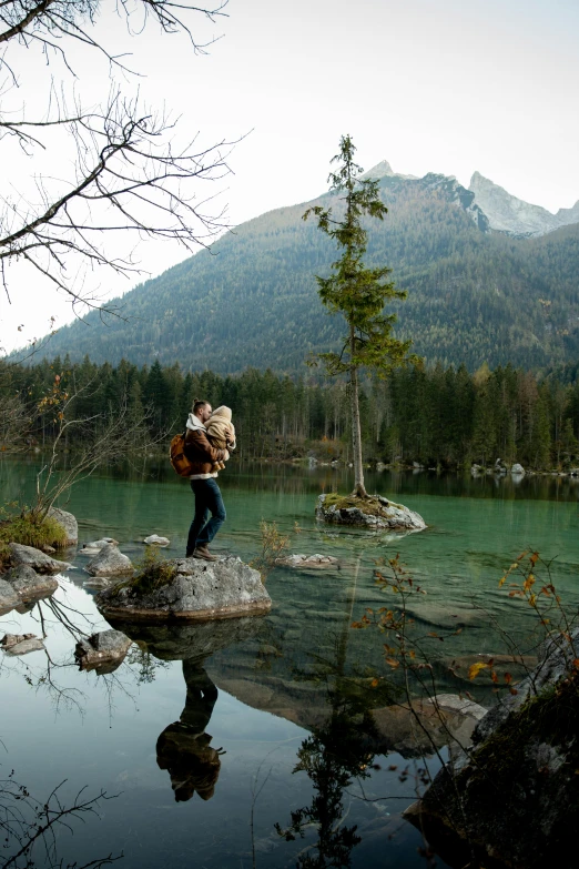 a man standing on top of a rock next to a lake, couple kissing, green waters, urs fischer, on location