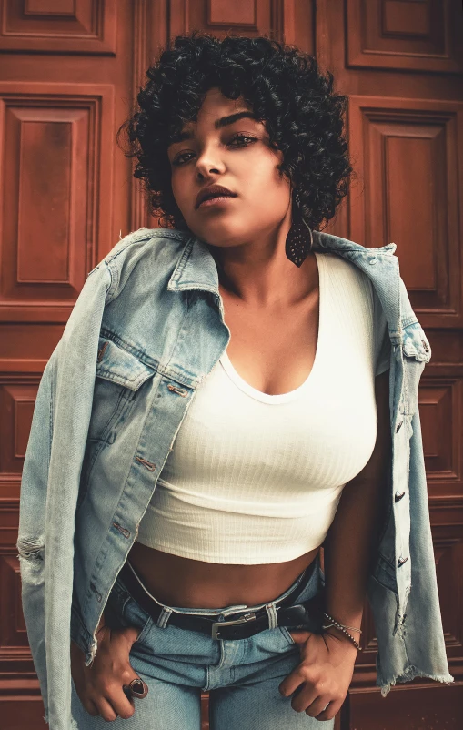 a woman standing in front of a wooden door, an album cover, trending on pexels, renaissance, jean jacket, croptop, curvaceous. detailed expression, mixed race woman