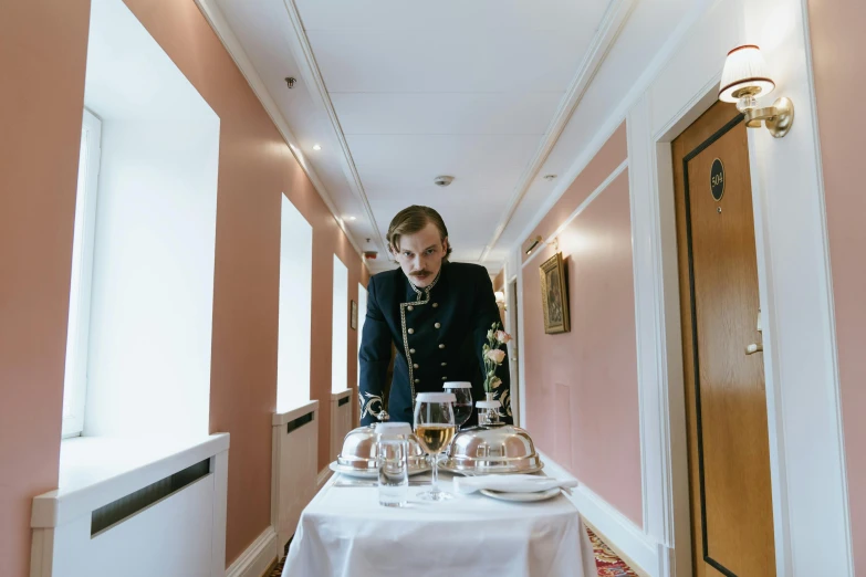 a man standing at a table in a hallway, by Emma Andijewska, unsplash, private press, princess at a royal banquet, wearing rr diner uniform, from the grand budapest hotel, plating