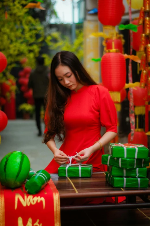 a woman in a red dress standing next to a table, pexels contest winner, happening, colorful paper lanterns, holding gift, dang my linh, red and green