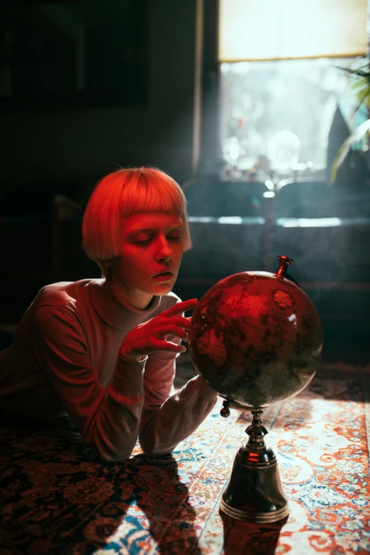 a woman sitting at a table with a globe in front of her, an album cover, inspired by Elsa Bleda, pexels contest winner, magic realism, bowl haircut, disco club of the occult, girl with short white hair, red and cinematic lighting