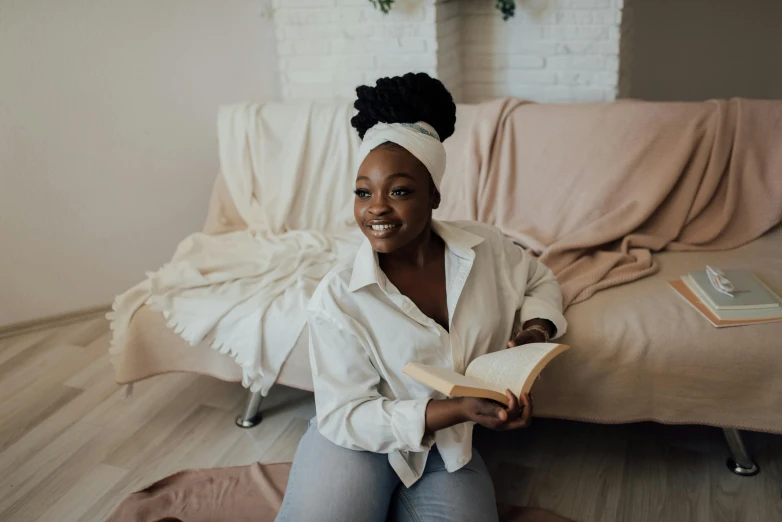 a woman sitting on a couch reading a book, a portrait, by Emma Andijewska, pexels contest winner, brown skin, white bed, smiling with confidence, wearing a headband