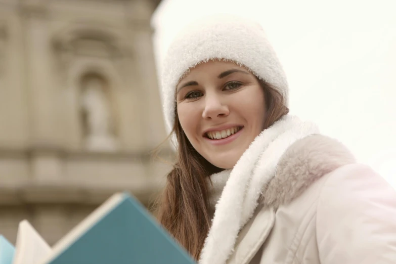 a woman is smiling while holding a book, by Alice Mason, pexels contest winner, wearing beanie, holiday, college, french girl