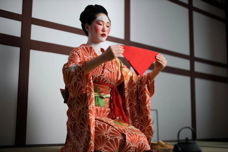 a woman in a kimono sitting on the floor, inspired by Goyō Hashiguchi, trending on unsplash, performing on stage, square, ornate mask and fabrics, red cloth around his shoulders