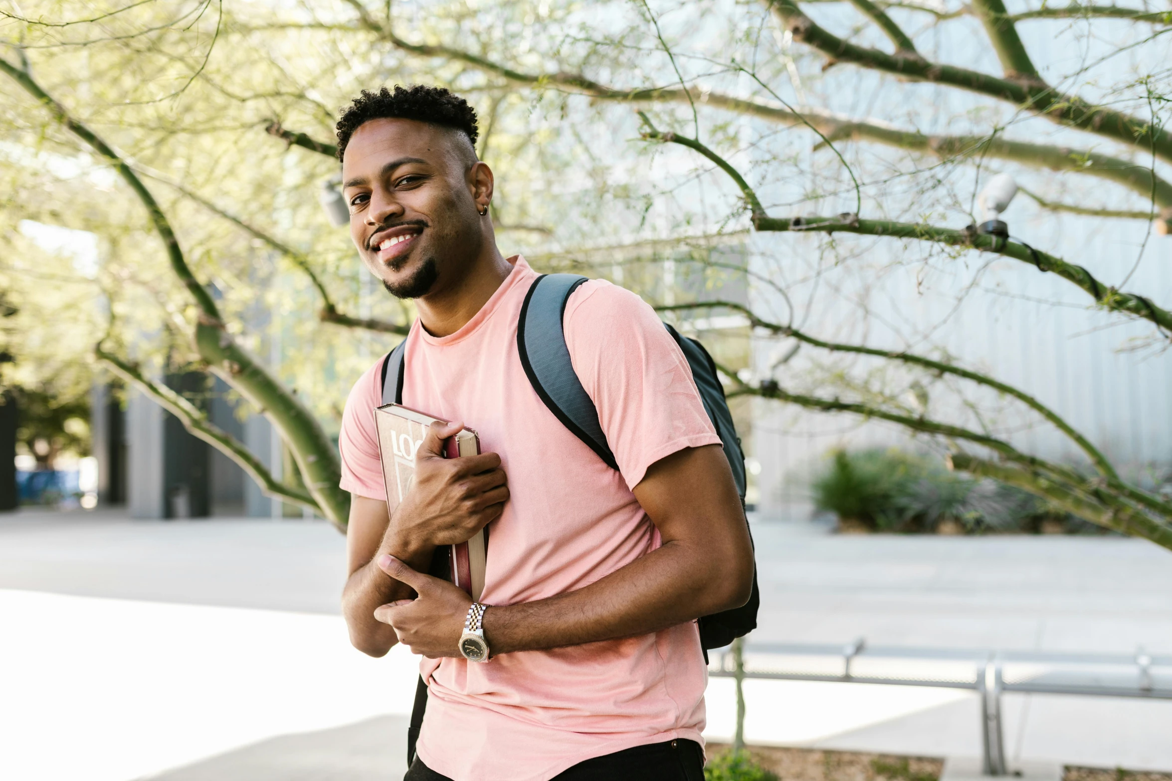 a man in a pink shirt standing next to a tree, by Carey Morris, pexels contest winner, with a backpack, jaylen brown, at college, smiling male