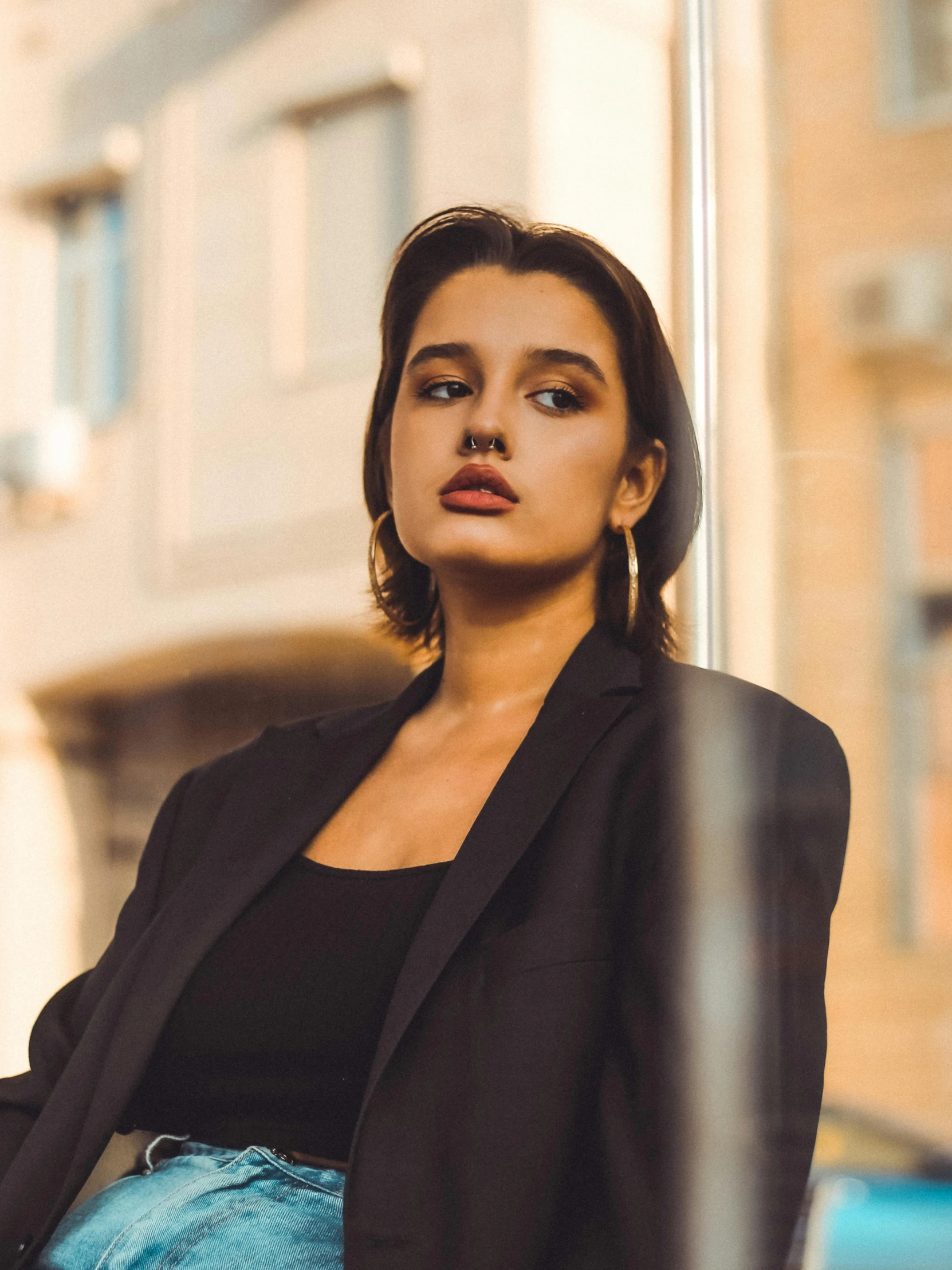 a woman leaning against a pole in front of a building, trending on pexels, young female in black tuxedo, portrait sophie mudd, androgynous face, black jacket | shiny