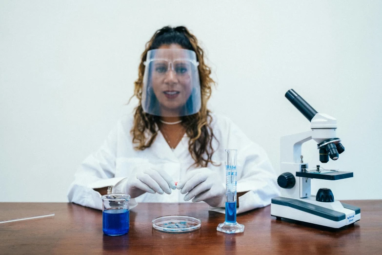 a woman sitting at a table in front of a microscope, pexels contest winner, wearing nanotech honeycomb robe, tanned ameera al taweel, blue scales with white spots, scientific glassware