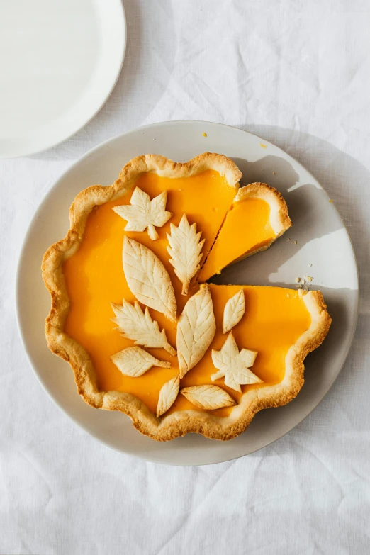 a pie sitting on top of a white plate, inspired by Elsa Beskow, shutterstock contest winner, yellow-orange, diecut, leafs, cut-away