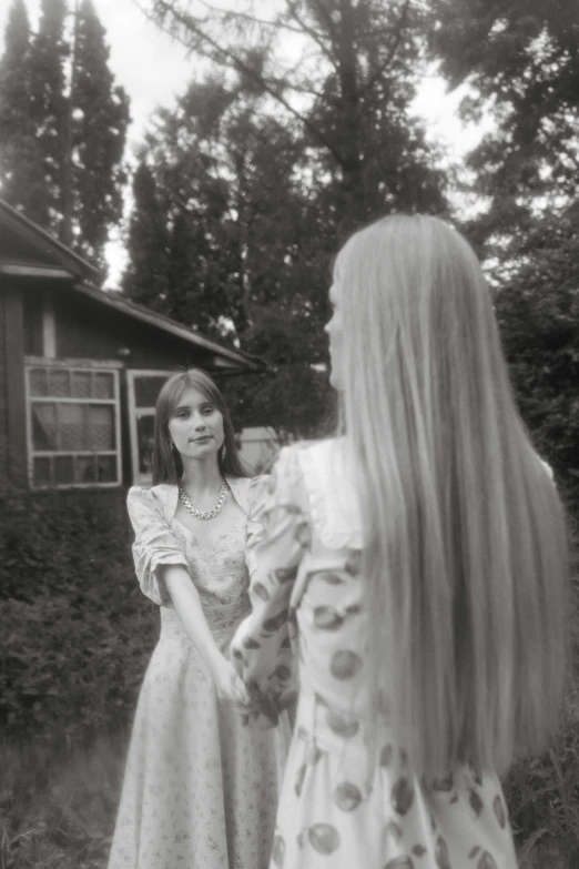 two women standing next to each other in front of a house, an album cover, inspired by Grethe Jürgens, conceptual art, extra long hair, ansel ], grainy photograph, midsummer