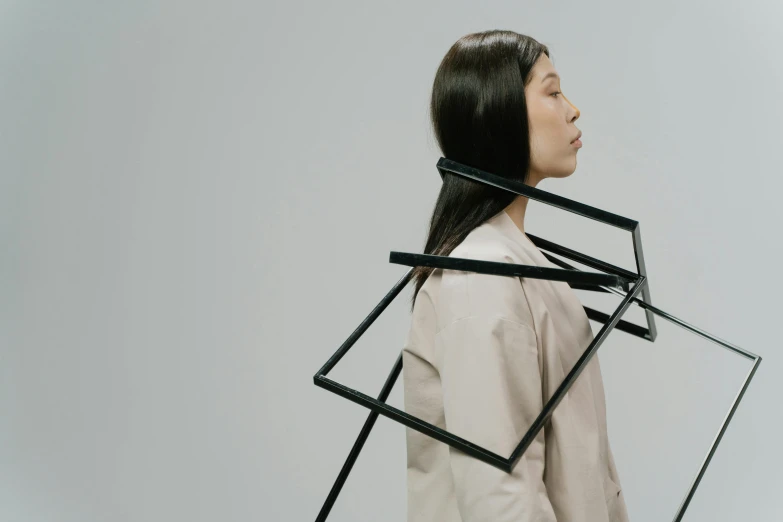 a woman standing in front of a white background, inspired by Kim Tschang Yeul, unsplash, kinetic art, square shapes, siting in a chair, wearing collar on neck, mechanical structure