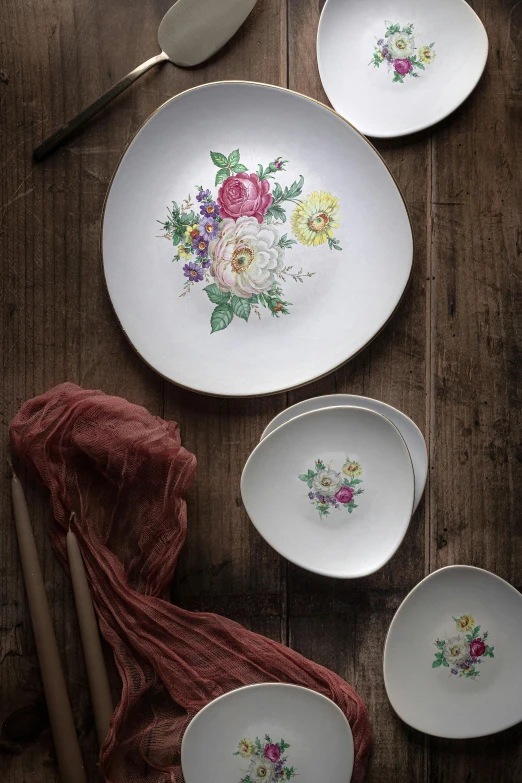 a table topped with plates and utensils on top of a wooden table, inspired by Ludwig Mestler, baroque, patchy flowers, detailed product image, vintage soft grainy, square