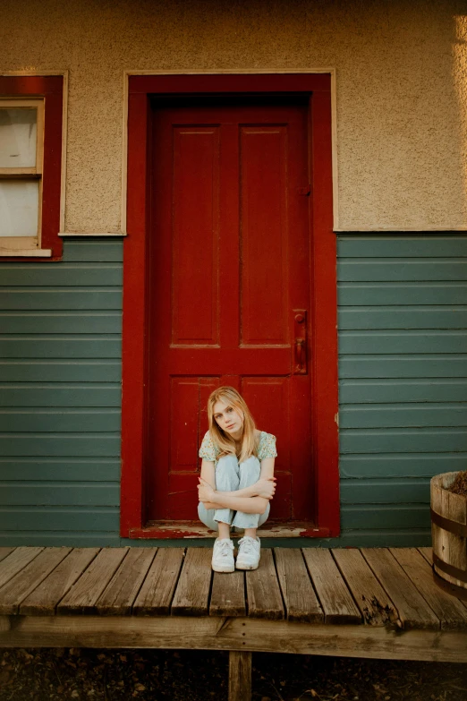 a girl sitting on a porch in front of a red door, an album cover, pexels contest winner, erin moriarty, sad expression, denim, full frame image