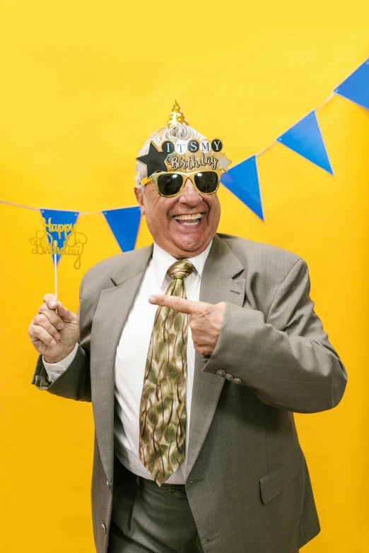 a man in a suit and tie holding a glass of champagne, wearing a party hat, blue and yellow theme, an oldman, photo booth