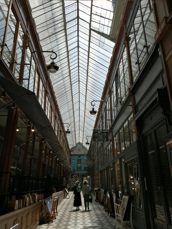 a couple of people that are walking in a building, old shops, skylights, painted metal and glass, you can see all the passageways