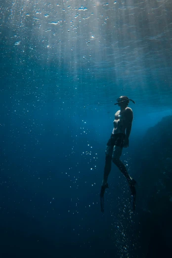 a person swimming in a body of water, standing under the sea, looking off into the distance, scuba diving, black depths