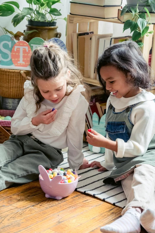 two little girls sitting on the floor playing with toys, inspired by Elsa Beskow, pexels contest winner, happening, holding in the hands easter eggs, m & m candy dispenser, app, board games on a table