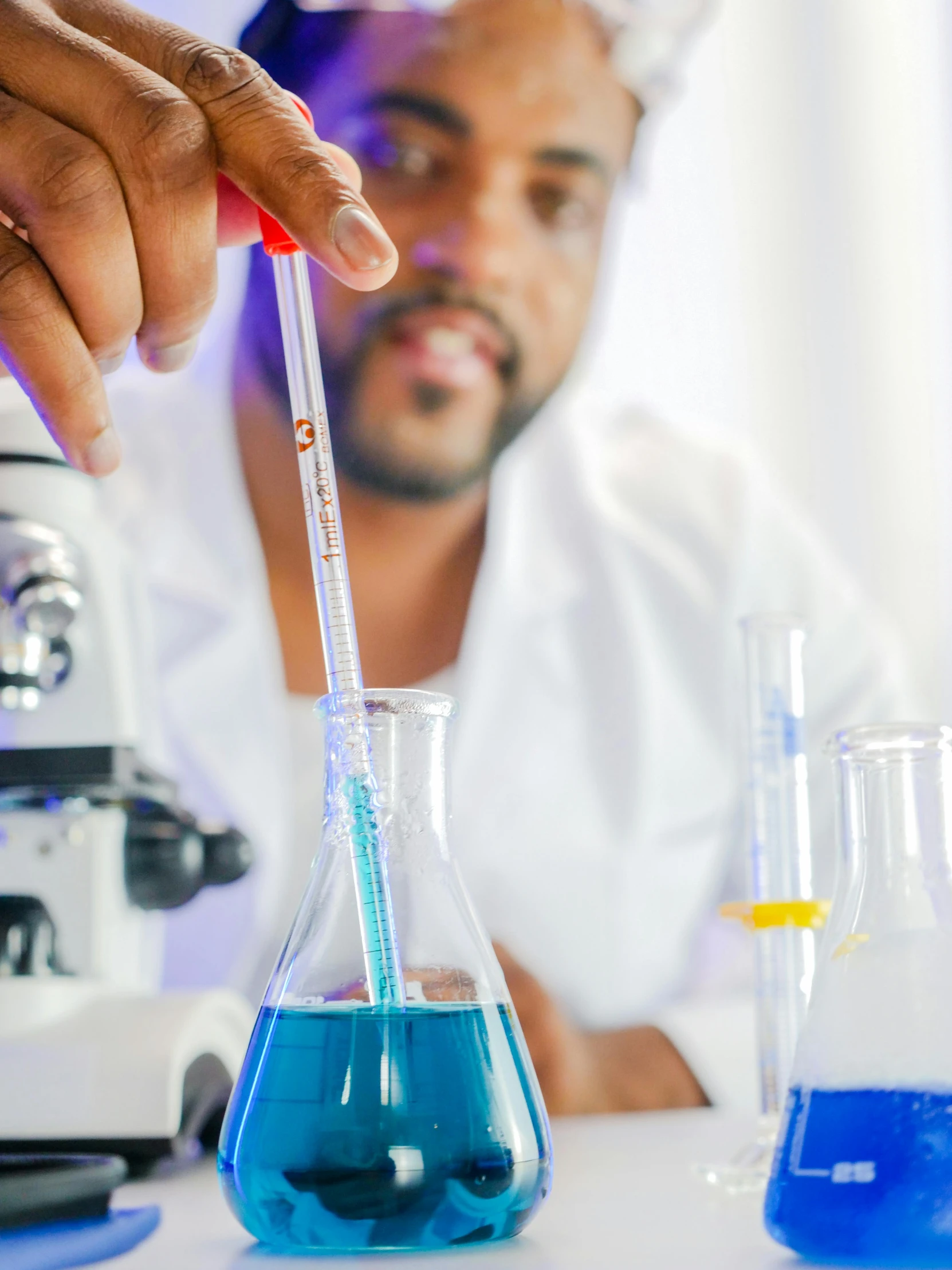 a man sitting at a table in front of a microscope, beakers of colored liquid, holding a blue lightsaber, profile image, trending photo