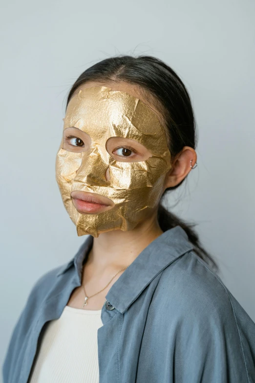 a woman wearing a gold face mask, by Julia Pishtar, korean face features, teenage girl, clear [bronze] face, manuka